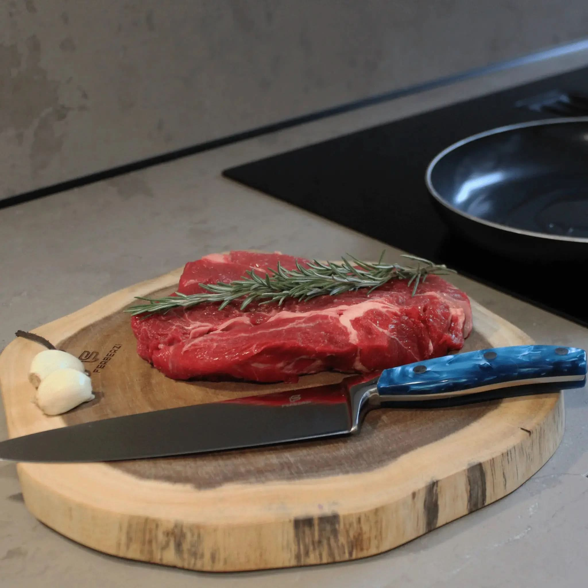 Koksmes met blauw acryl handvat op acaciahouten snijplank met steak en knoflook