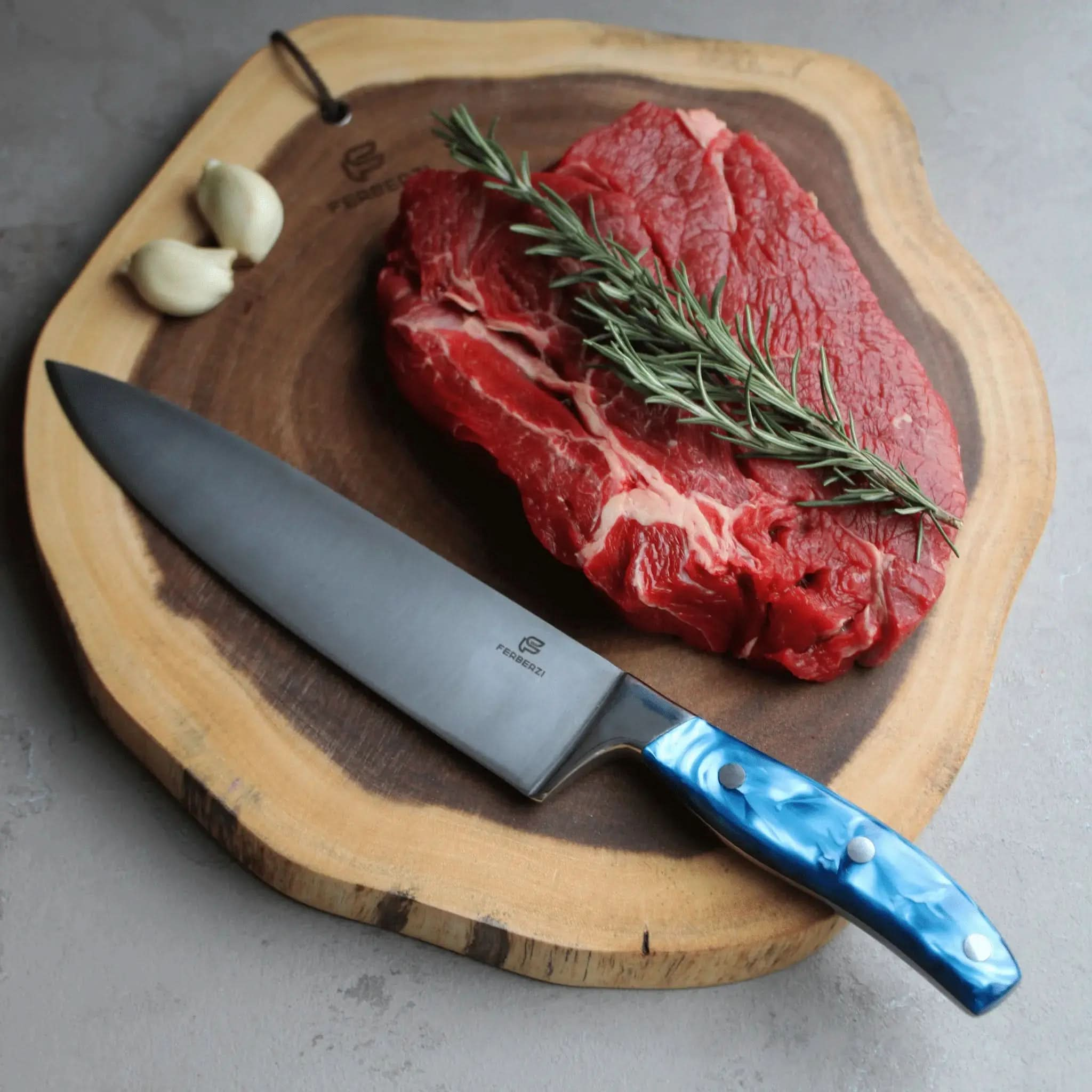 Koksmes met blauw acryl handvat op acaciahouten snijplank met steak en rozemarijn