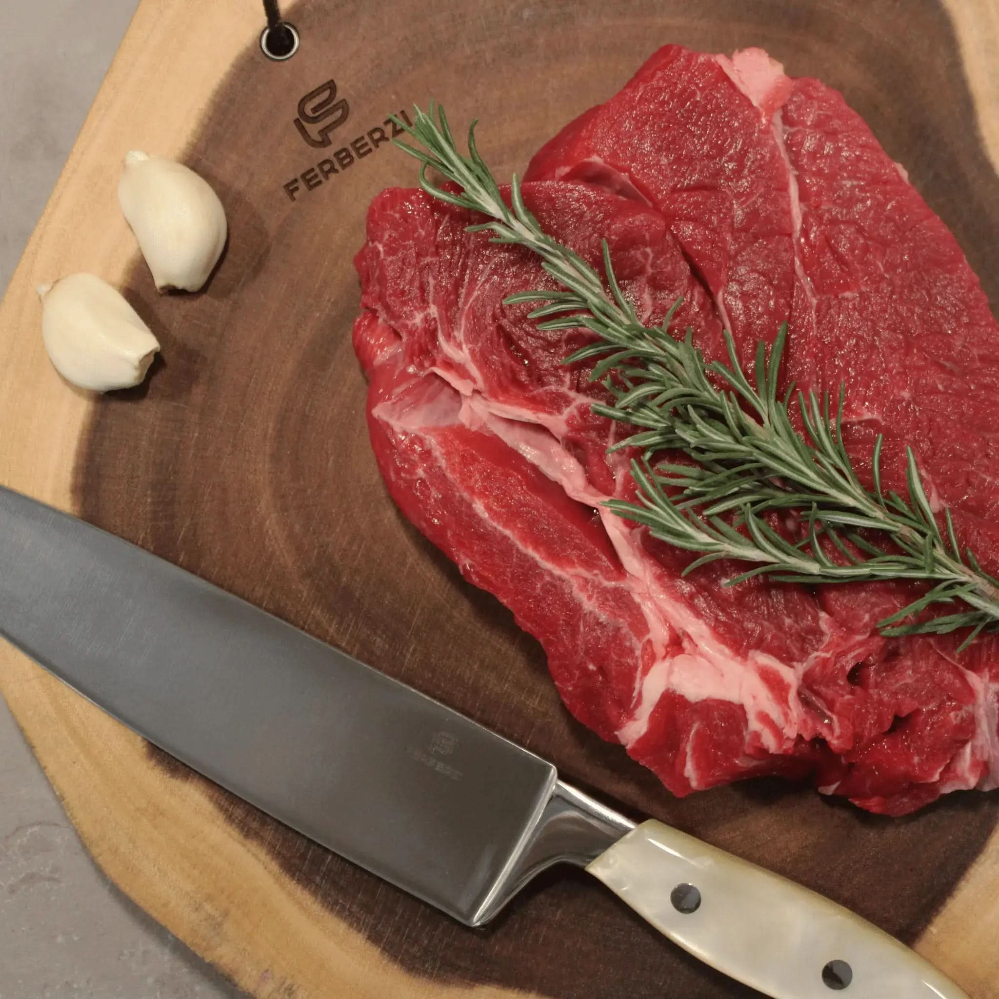 Koksmes met parelwit acryl handvat op acaciahouten snijplank met steak en rozemarijn
